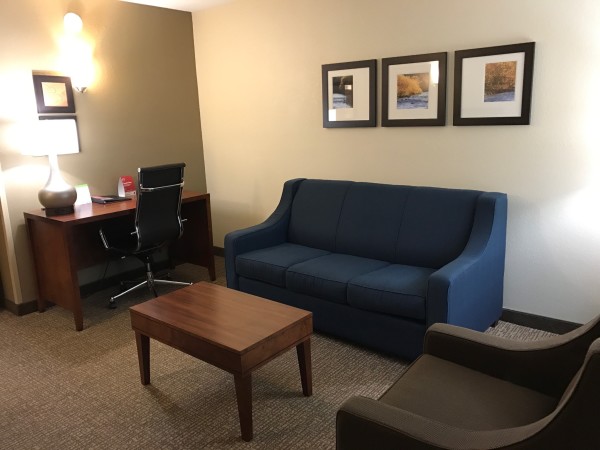 The front living area in the Comfort Suites room is spacious and includes couch, sitting chair, tv, and computer desk.